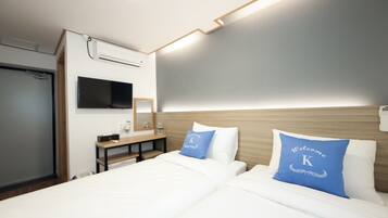 A hotel room with two beds, a flat-screen TV, a wooden headboard, and a bedside table with a mirror and a lamp.