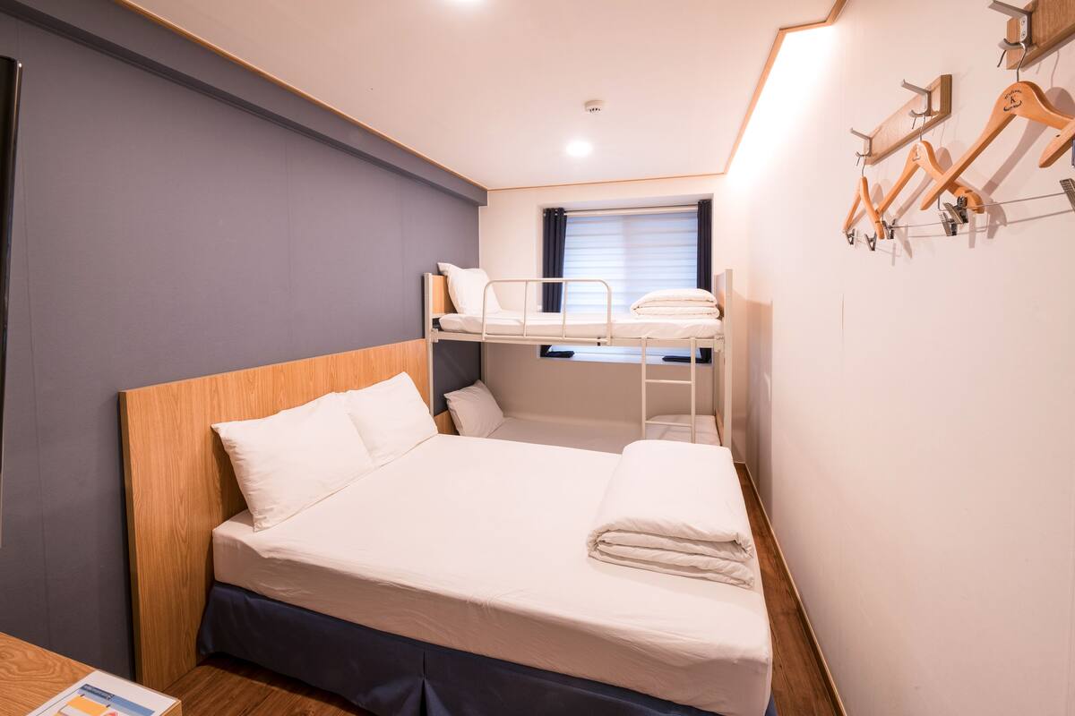 A bunk bed room with a wooden headboard, a desk, and a window with curtains.