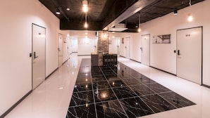 Un hall d’hôtel moderne avec un sol en marbre noir poli, des murs blancs et des portes numérotées.
