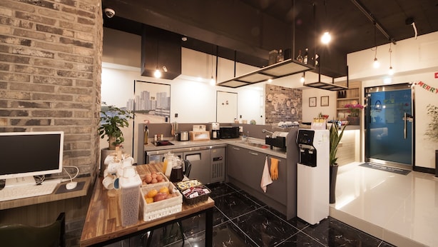 Une cuisine moderne avec un mur en briques, un coin repas doté d ’une table en bois et un réfrigérateur orné d’une inscription « Joyeux ».