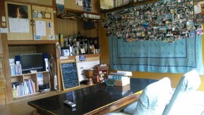 A cozy room with a wooden bookshelf, a coffee machine, and a wall decorated with photos. - OKINAWA MOTOBU GUESTHOUSE - Hostel (Motobu)