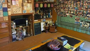 A cozy room with wooden walls, a clock, various books, a television, and a wall covered with photos. - OKINAWA MOTOBU GUESTHOUSE - Hostel (Motobu)