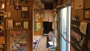 A narrow hallway with wooden walls, a fan, and various items on display including framed pictures and a bulletin board with flyers. - OKINAWA MOTOBU GUESTHOUSE - Hostel (Motobu)