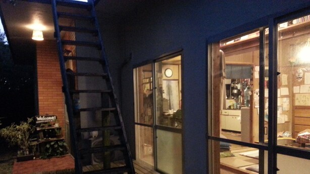 A wooden deck with a ladder leading to a glass door entrance. - OKINAWA MOTOBU GUESTHOUSE - Hostel (Motobu)
