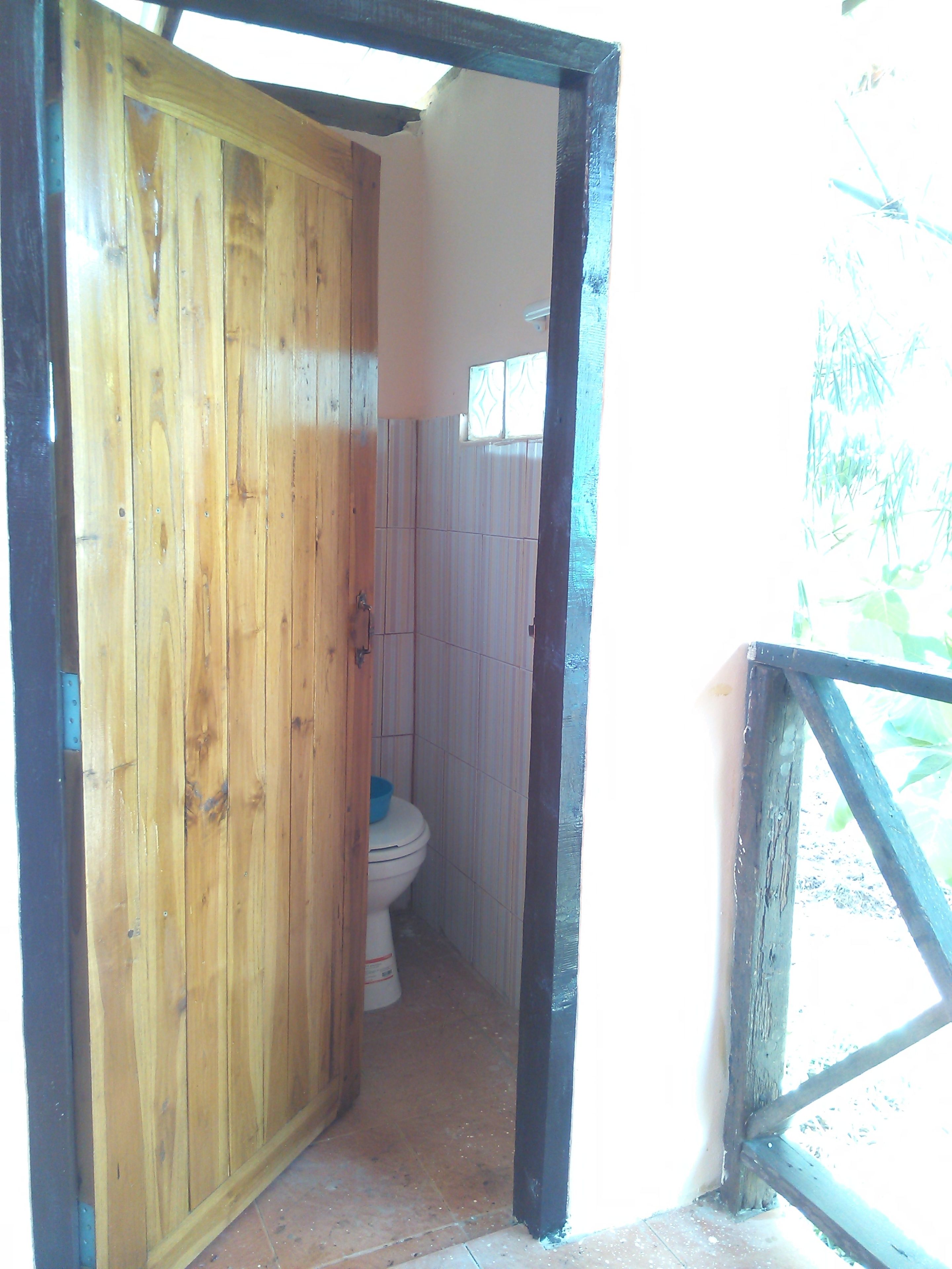 Puerta de madera que da a un baño pequeño con inodoro y ventana.