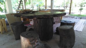 Une table rustique en bois, dotée d’un aspect naturel et vieilli, soutenue par quatre larges pieds en forme de troncs d’arbres.