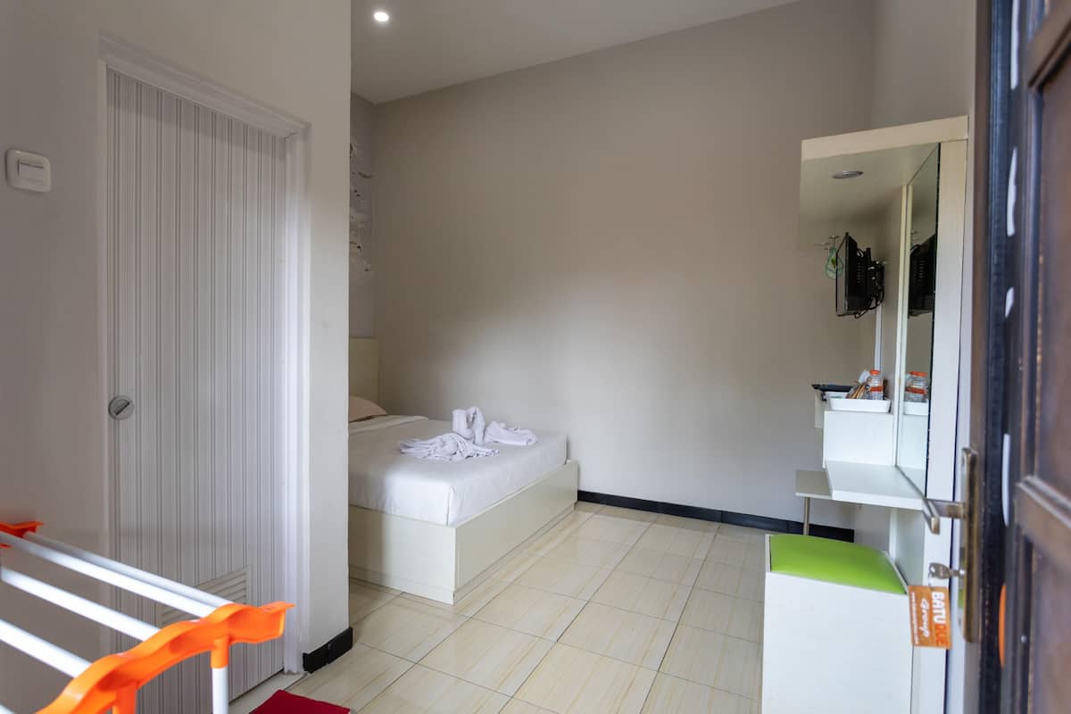 Habitación de hotel con cama, armario blanco, baño con espejo y un estante pequeño con artículos de aseo.