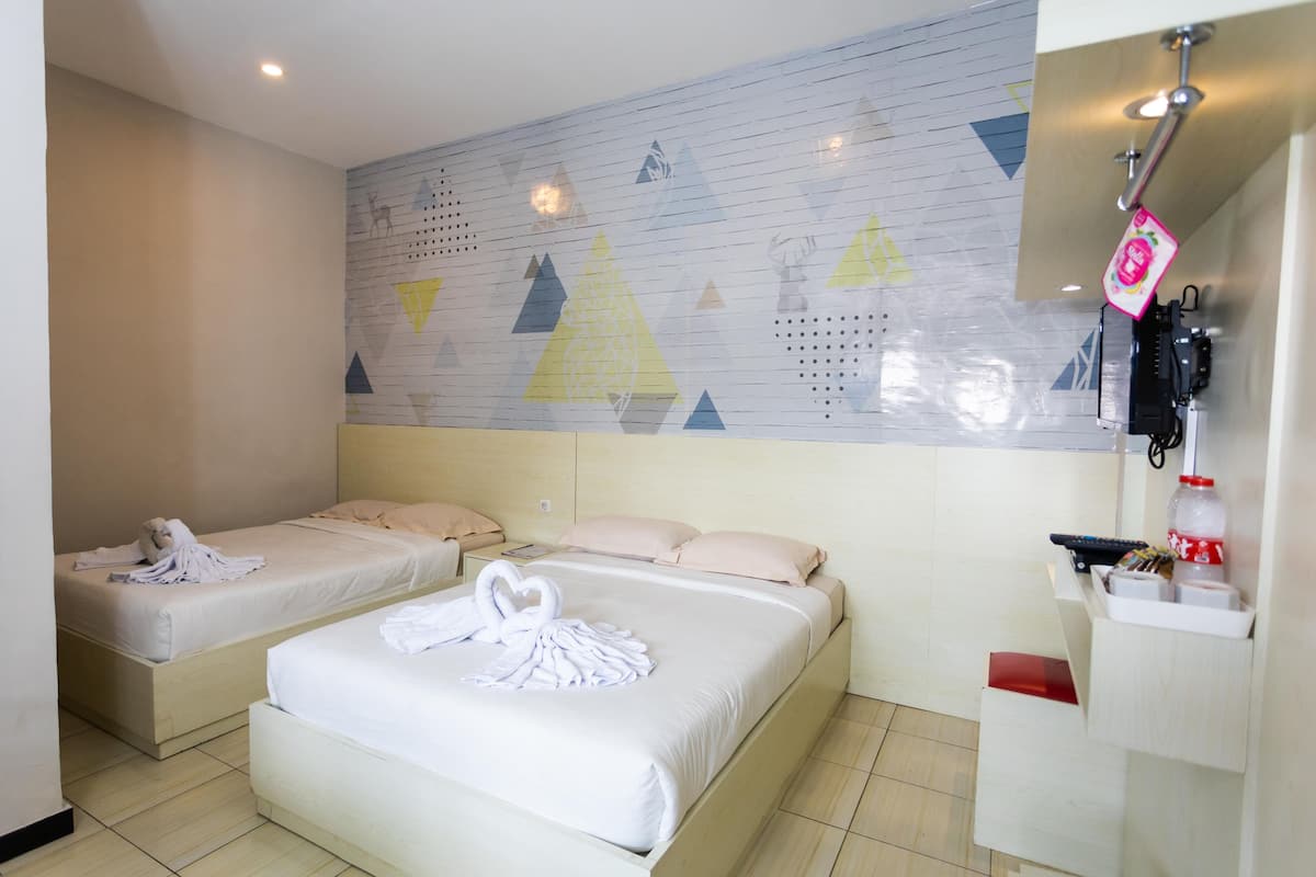 Habitación de hotel con dos camas individuales, una pared con patrones geométricos, un pequeño estante con artículos de aseo y un panel de control en la pared.
