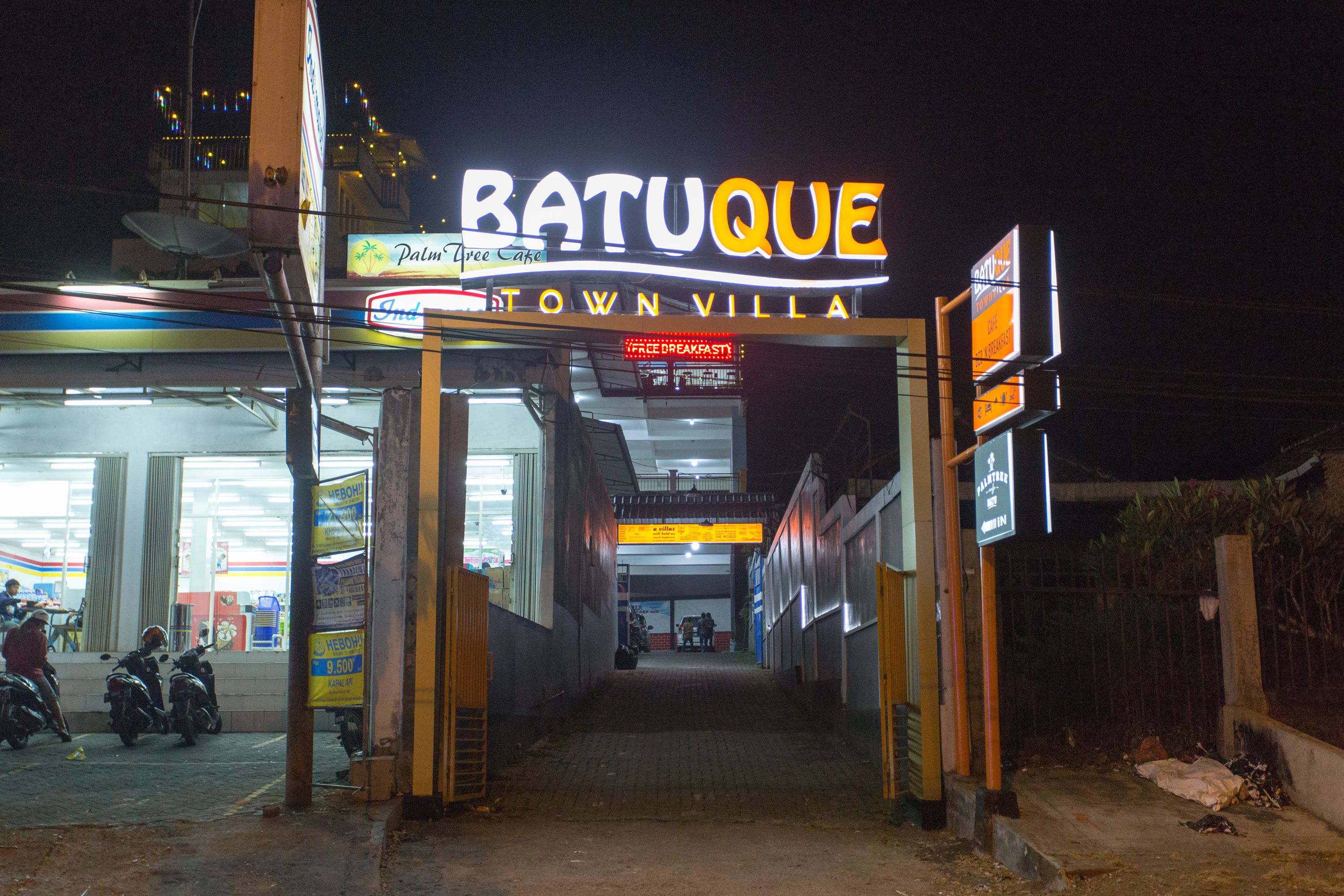 A Bantuque Town Villa with a neon sign, a visible entrance, and a few parked motorcycles outside.