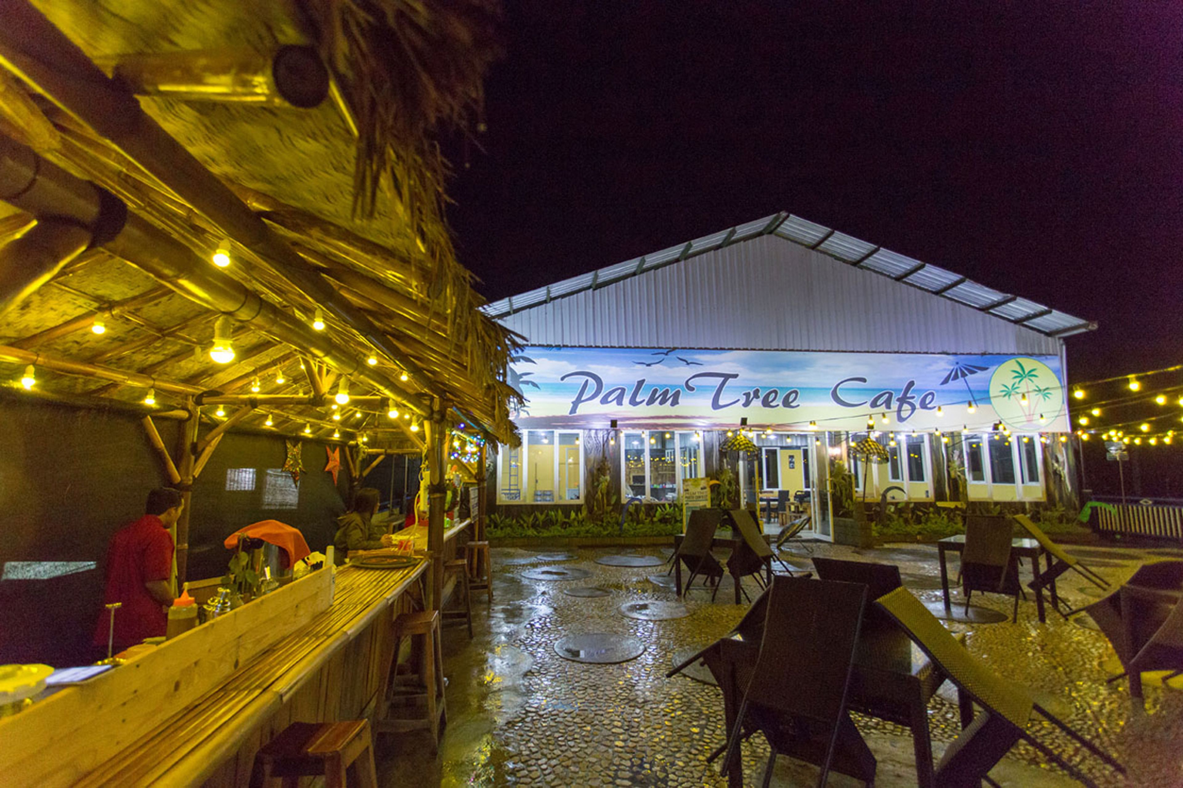 An outdoor seating area with tables and chairs, a covered patio, and a building with a sign reading "Palm Tree Cafe."