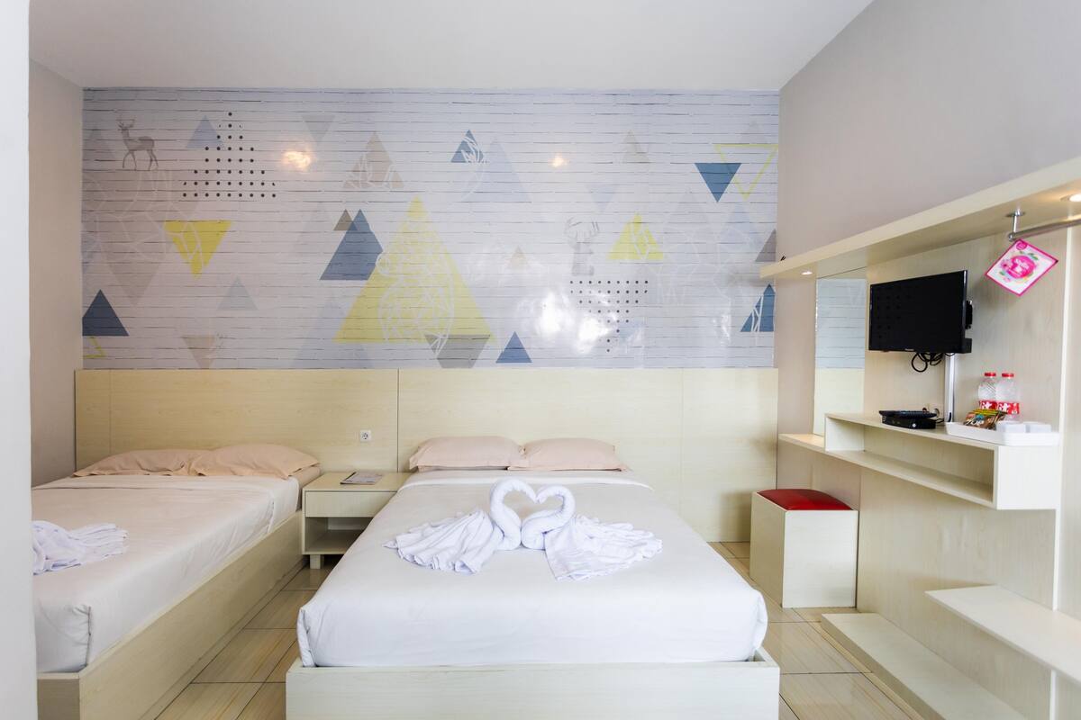 Habitación de hotel con dos camas, una pared con diseños geométricos, un televisor y un estante pequeño con objetos.