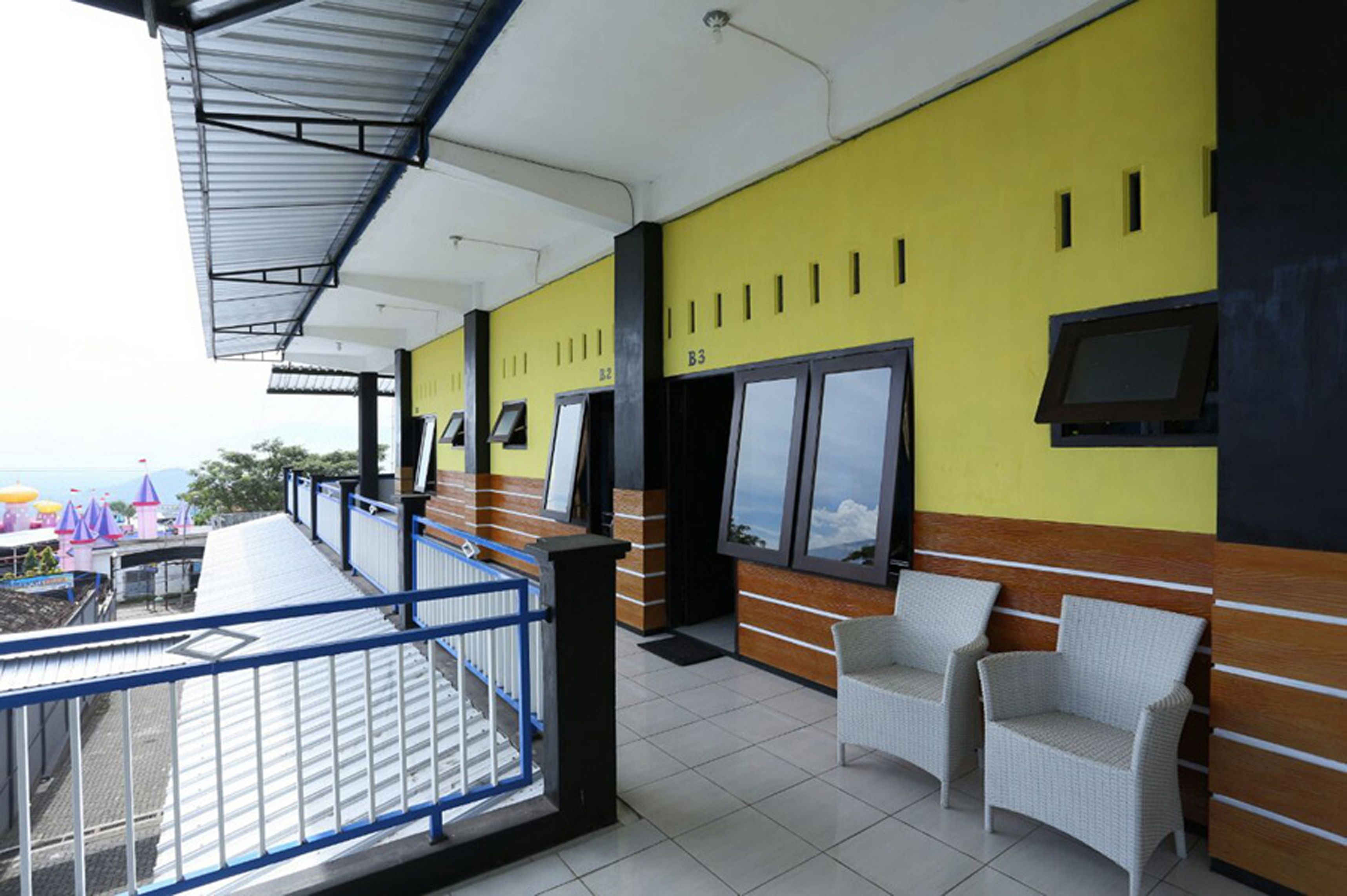 Un espace extérieur abrité, avec des sièges, un mur jaune et noir, un écran de télévision et des chaises en osier.