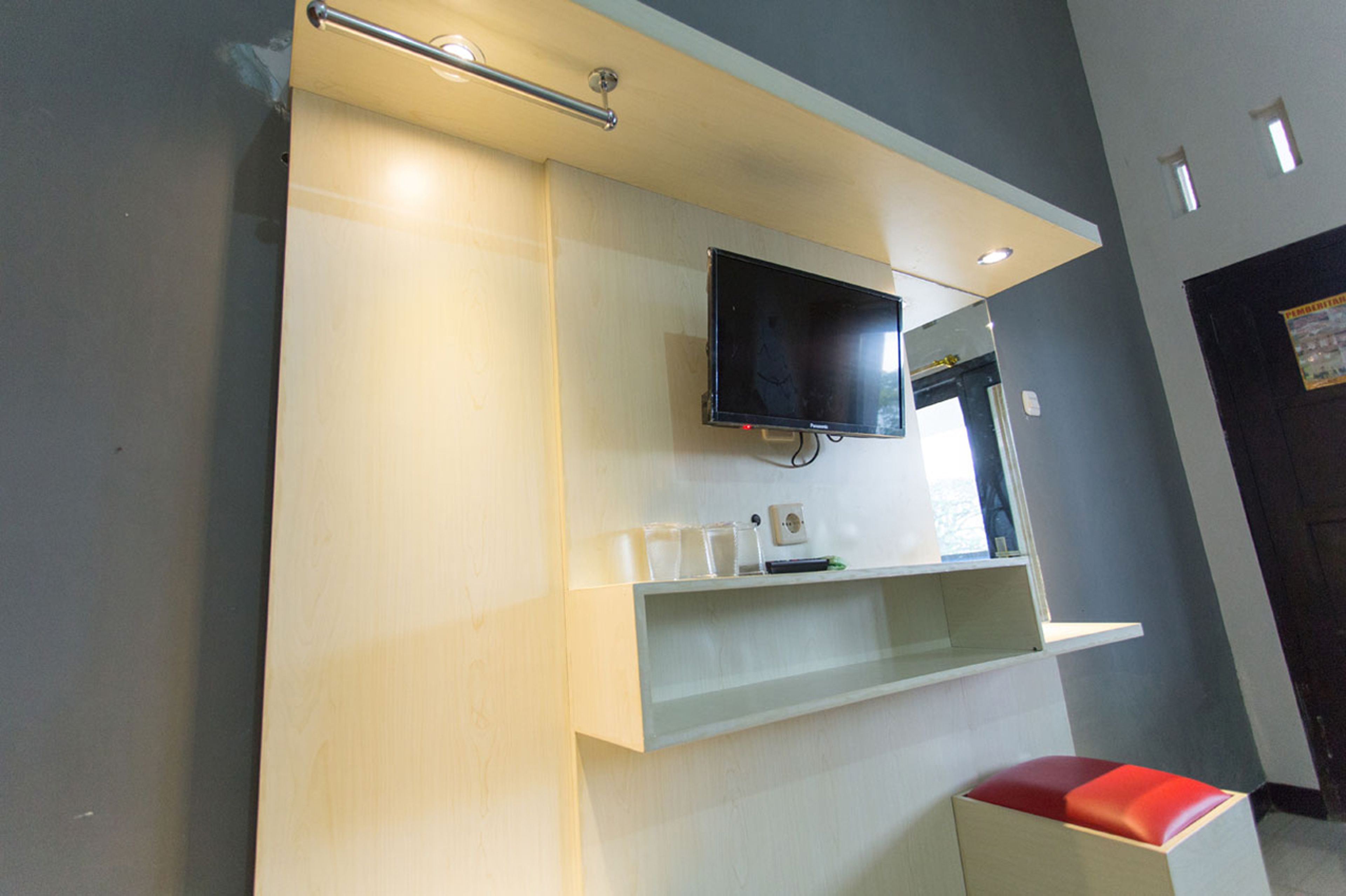 A modern bathroom with a mounted TV, a shelf with toiletries, and a red bench.