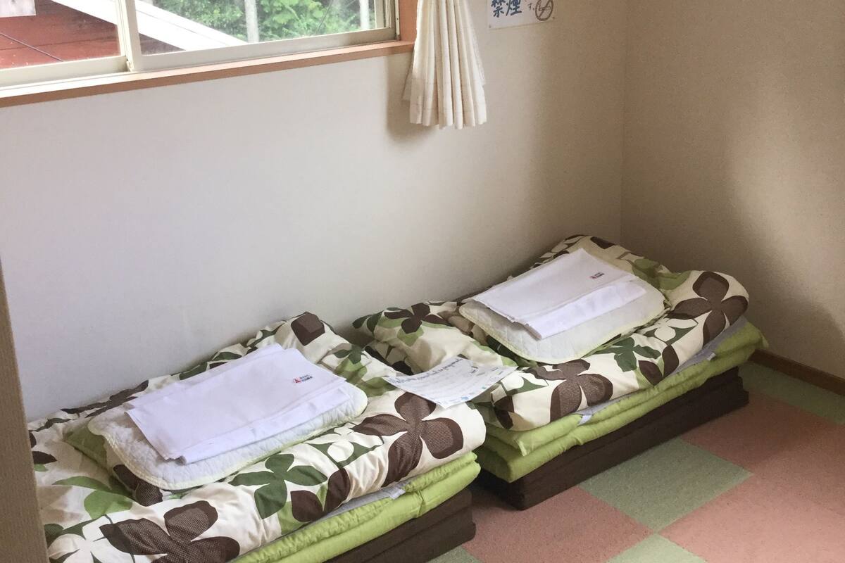 Una habitación pequeña con dos camas individuales, una ventana con cortinas, un cartel de 'No fumar' y un cuadrado amarillo en la pared.