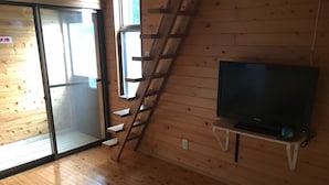 Ein Holzinnenraum mit einem Fernseher auf einem Standfuß, einer Schiebetür und einer Holztreppe.