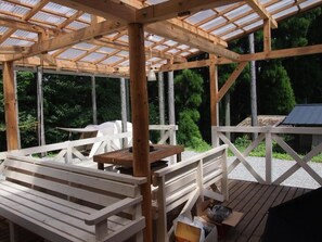 Een houten terras met een pergola, banken en een tafel.