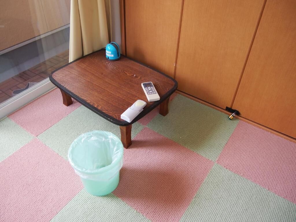 A small wooden table with a remote control and a plastic container on a checkered floor.
