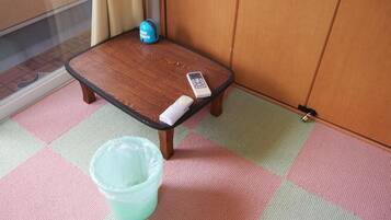 A small wooden table with a remote control and a plastic container on a checkered floor.