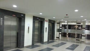 Un espace moderne abritant trois ascenseurs, avec un sol carrelé et une barrière métallique.
