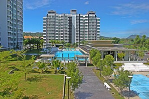 Un hotel moderno con una amplia piscina, varios balcones y abundante vegetación.