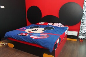 A bed with a Mickey Mouse themed bedspread, a black headboard, and a Mickey Mouse pillow.