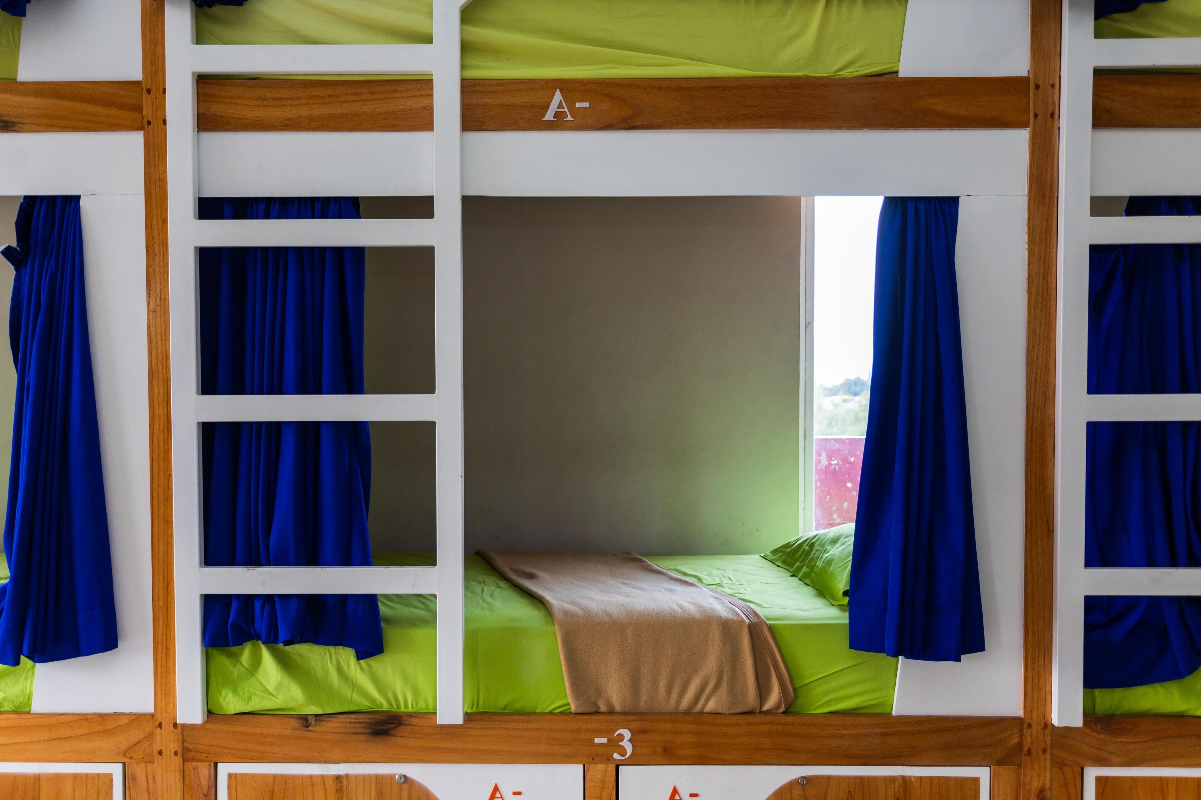 A bunk bed with a wooden frame, green bedding, and blue curtains.