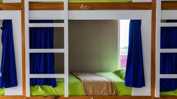 A bunk bed with a wooden frame, green bedding, and blue curtains.