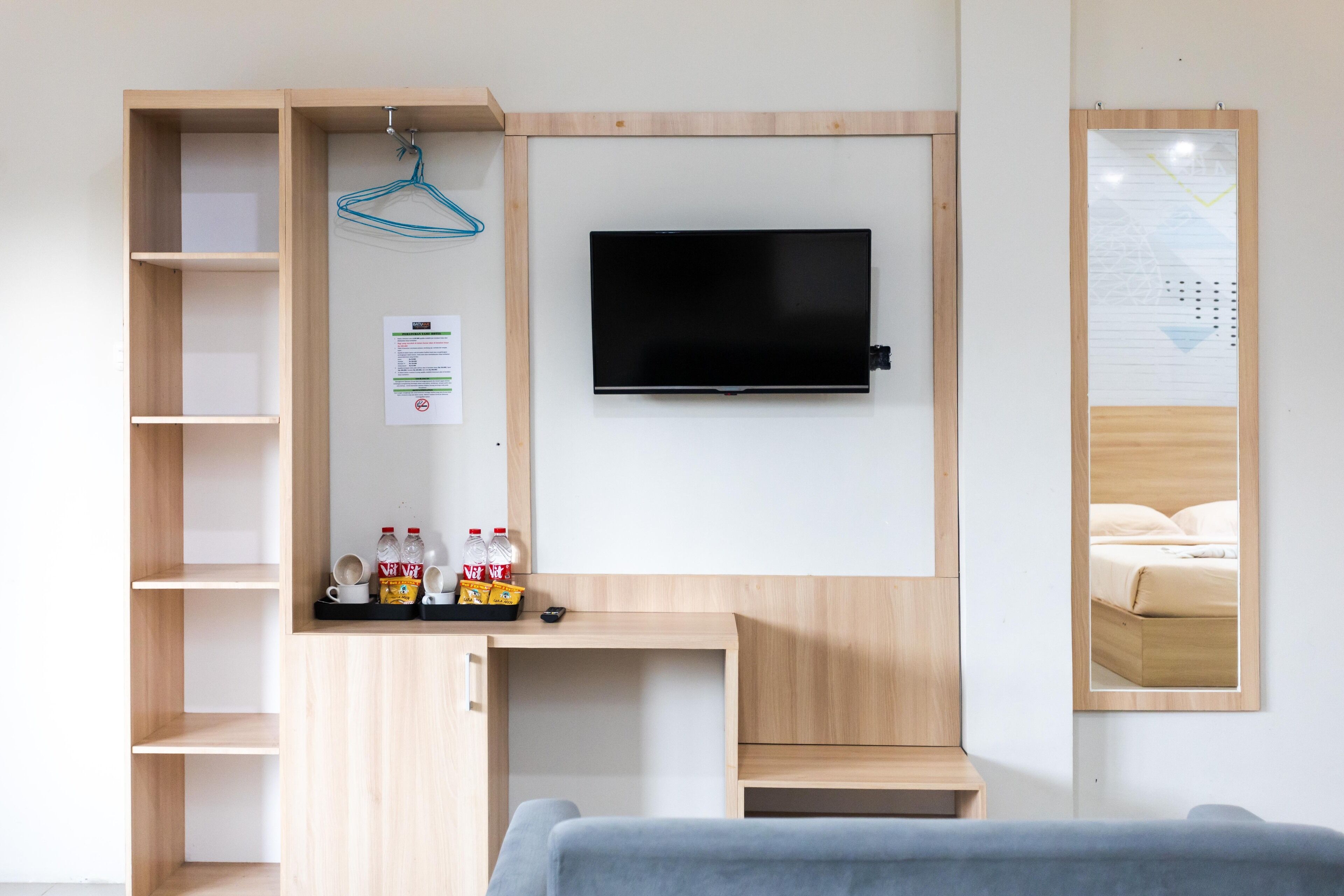 A modern room with a wooden desk, a mounted TV, and a mirror reflecting a bed.