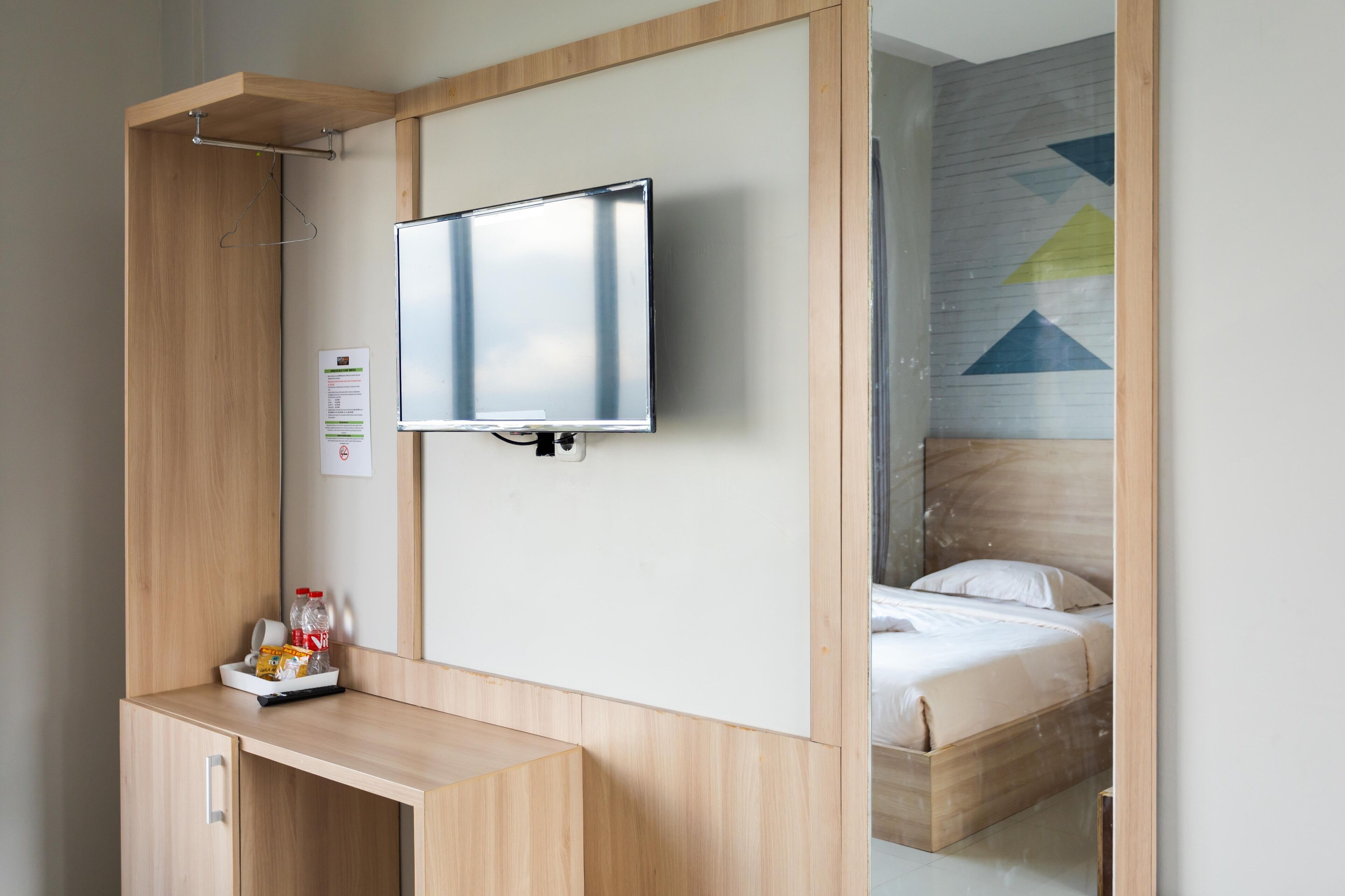 A hotel room with a bed, a TV mounted on the wall, a wooden desk with a tray of snacks, and a view of the room's interior.
