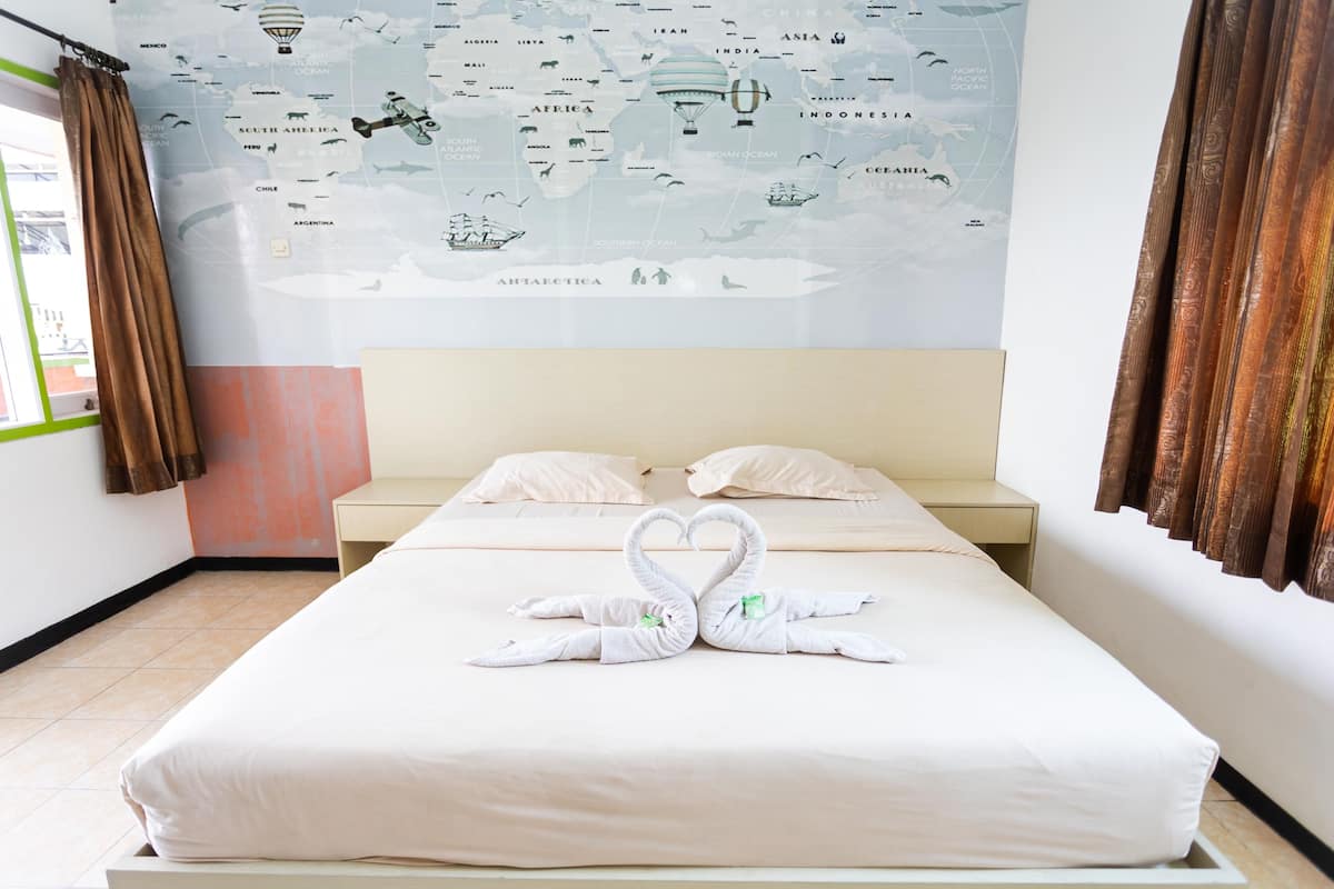 Una habitación de hotel con un gran mapa del mundo en la pared, una cama con ropa blanca y dos toallas con forma de cisne.