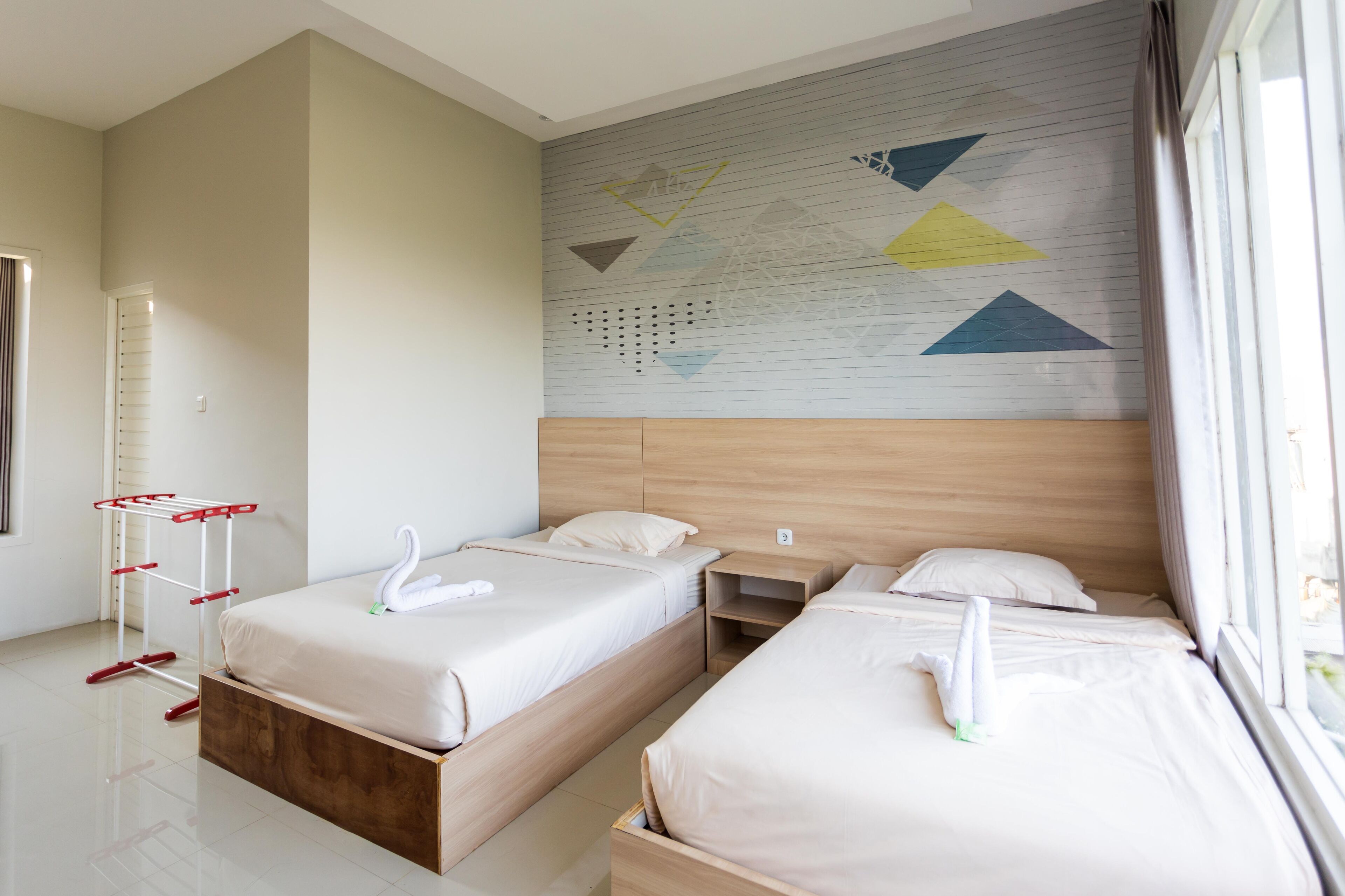 A hotel room with two beds, a wooden headboard, a wall art piece, and a window with curtains.