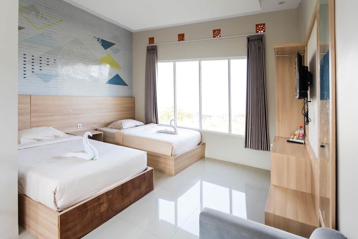 Habitación de hotel con dos camas, cabecero de madera, ventana grande con cortinas y televisor de pantalla plana montado en la pared, además de un escritorio de madera.