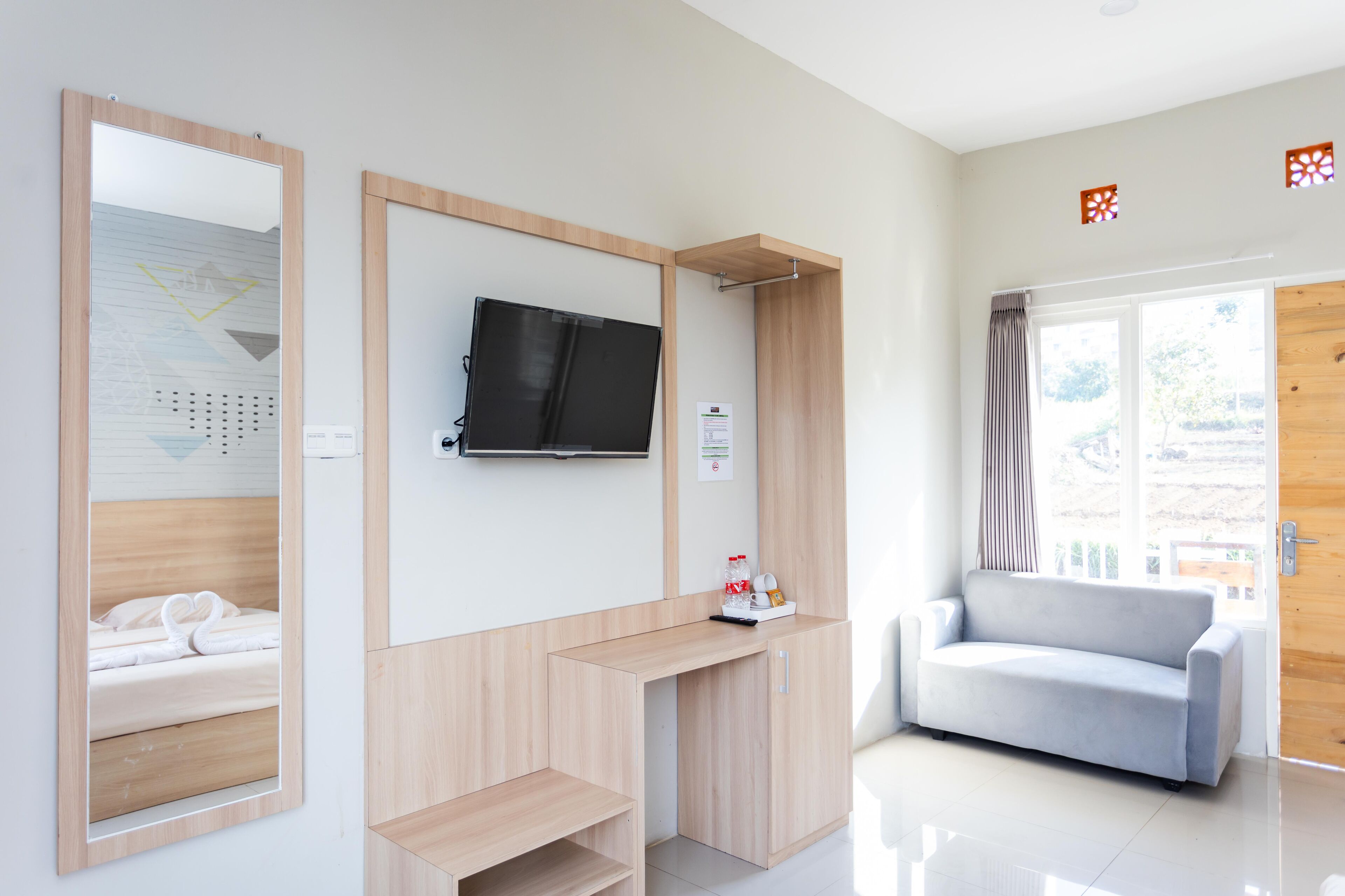 Een moderne hotelkamer met een houten bureau, een flatscreen televisie, een bank en een grote spiegel.