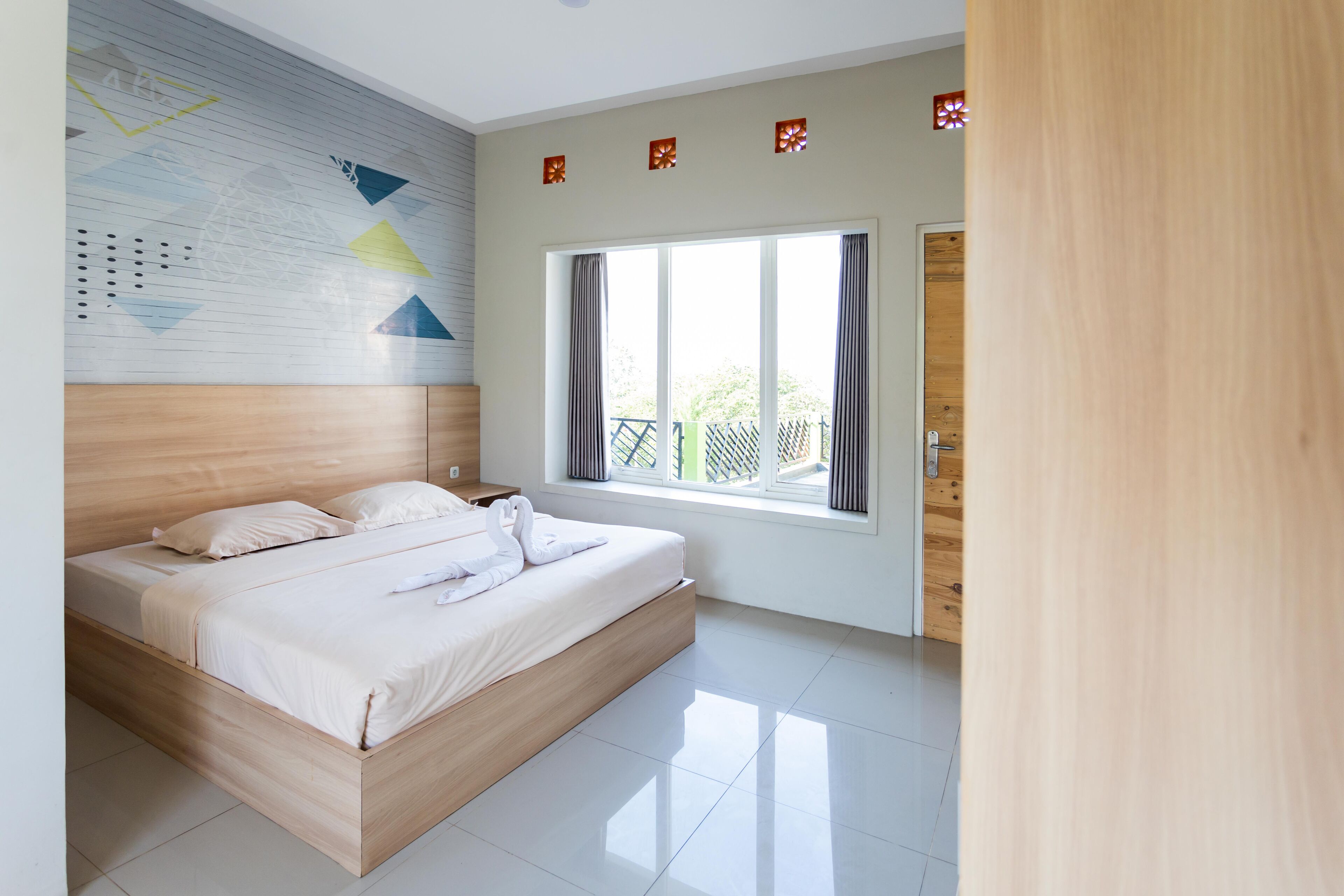 A modern bedroom with a wooden bed, a large window with curtains, and a wall with geometric patterns.