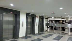 A modern elevator area with three elevators, a tiled floor, and a metal barrier. - Homestay Signature Suite (Sandakan)