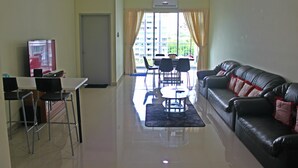 A living room with a black leather sofa, a dining table with chairs, a TV, and a ceiling fan. - Homestay Signature Suite (Sandakan)