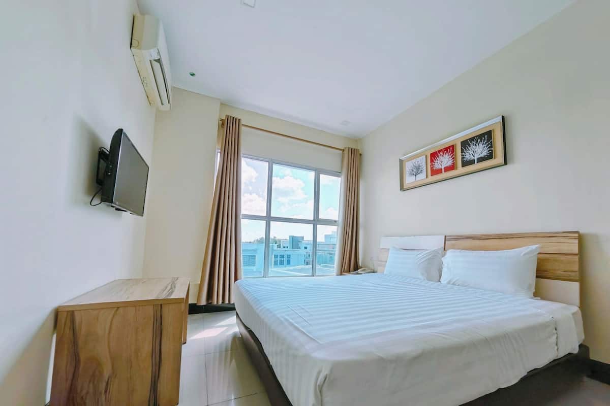 A hotel room with a bed, a TV, a window with curtains, and a framed picture on the wall.