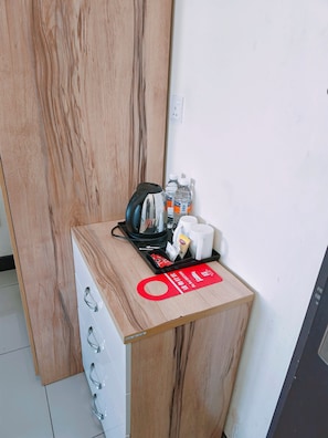 A wooden cabinet with a tray containing a kettle, water bottles, a coffee cup, and a red sign.