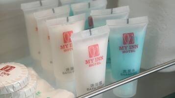Estante de hotel con artículos de baño, incluyendo espuma de baño, champú y un recipiente con sales de baño.