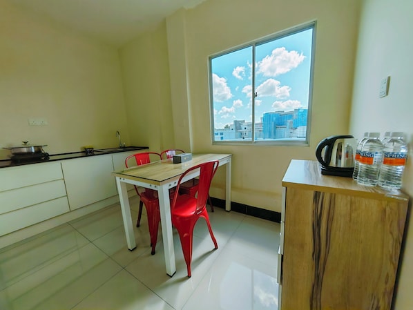 A small kitchen with a table and chairs, a window with a city view, and a cabinet with water bottles.