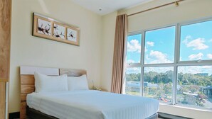 A hotel room with a large bed, a wooden headboard, a framed floral artwork, a telephone, and a large window offering a city view. - My Inn Hotel Kota Samarahan (Kota Samarahan)