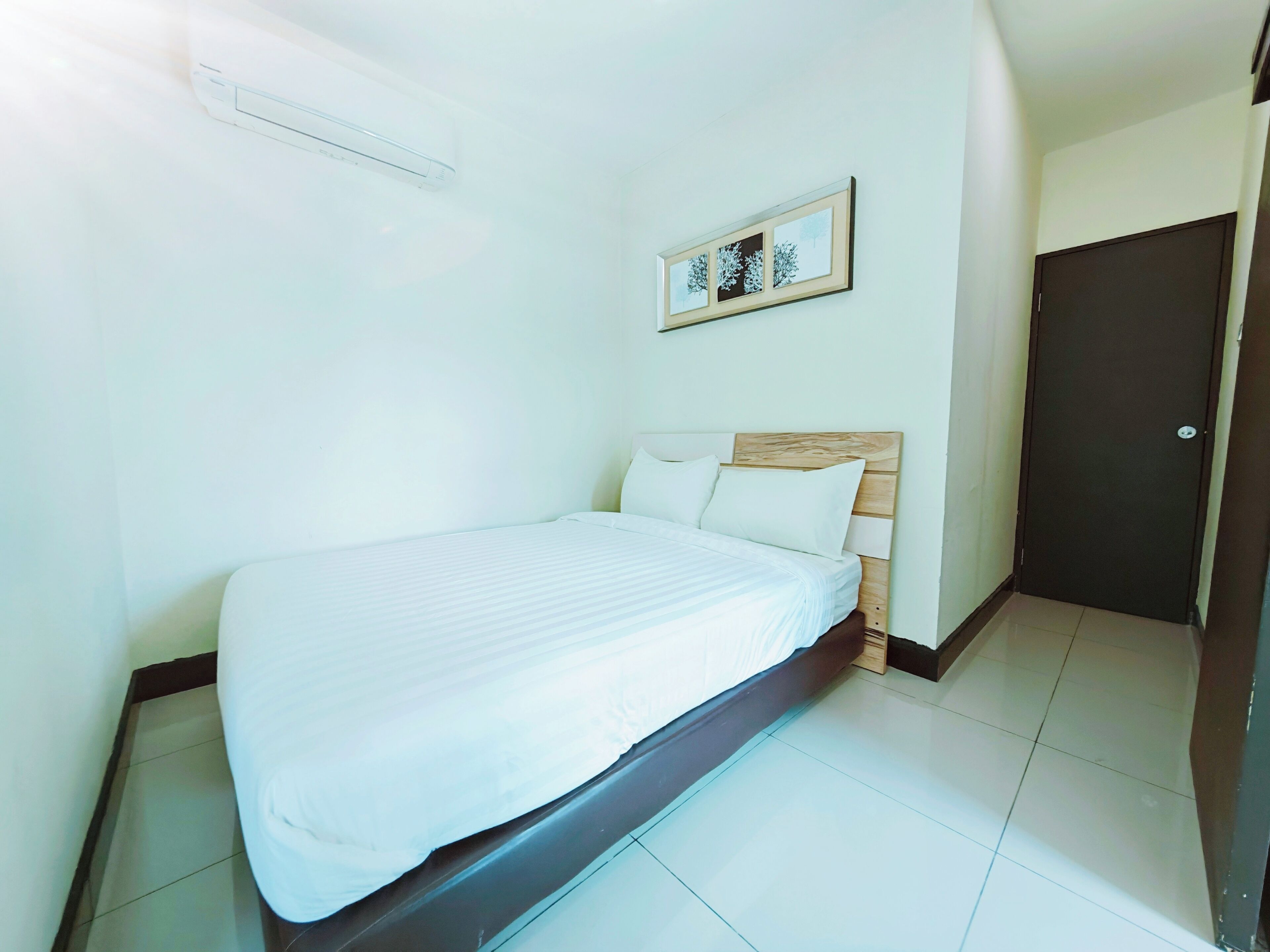 A hotel room with a bed, a framed picture on the wall, and a door.