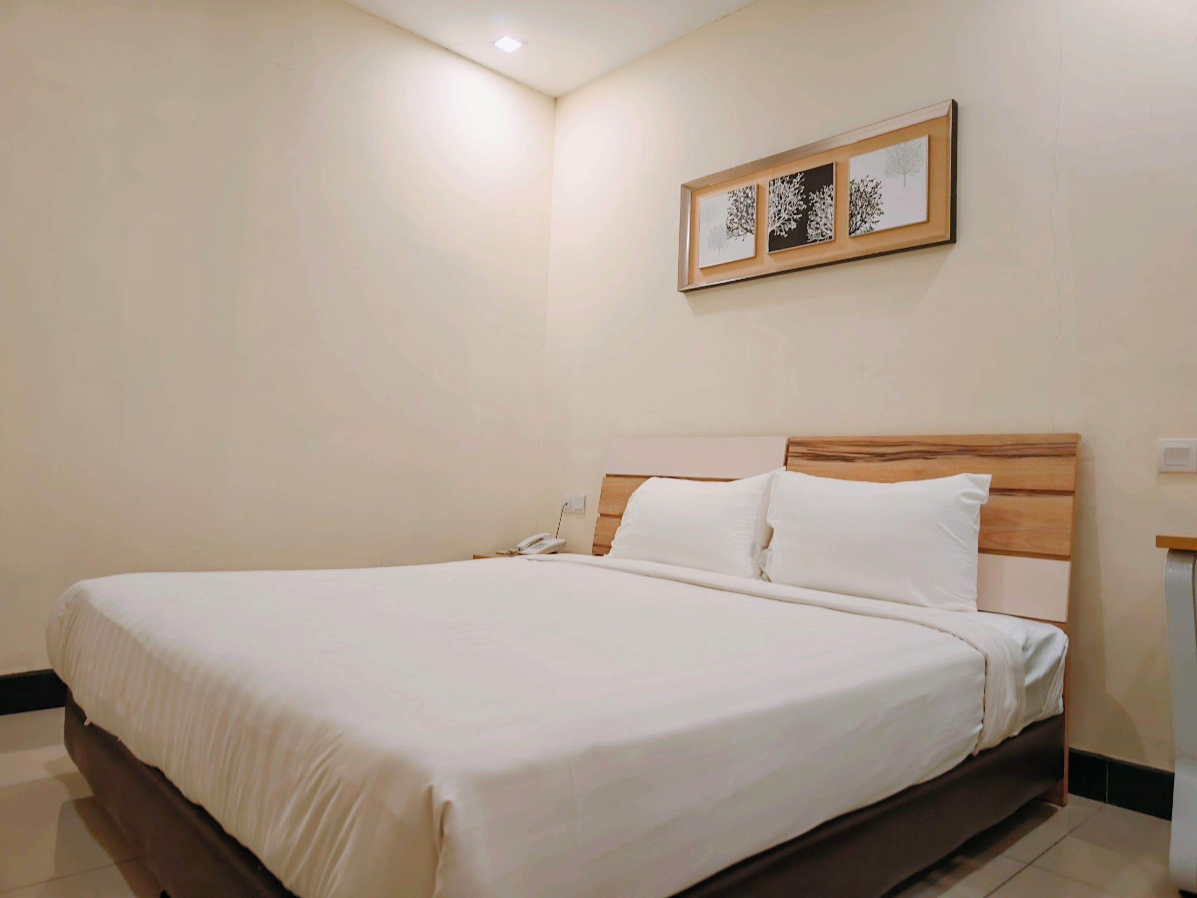 A neatly made bed with white linens, a wooden headboard, and a bedside table with a phone.