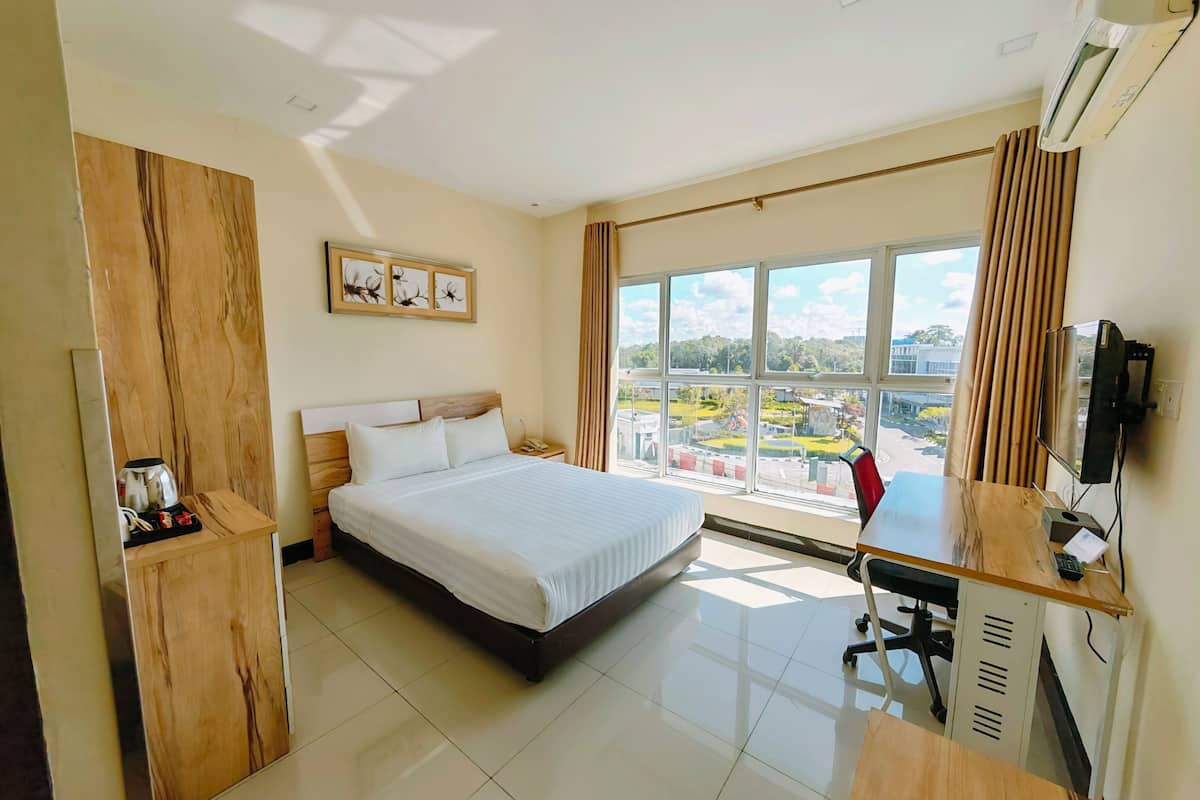 A hotel room with a bed, desk, TV, and a view of a cityscape.