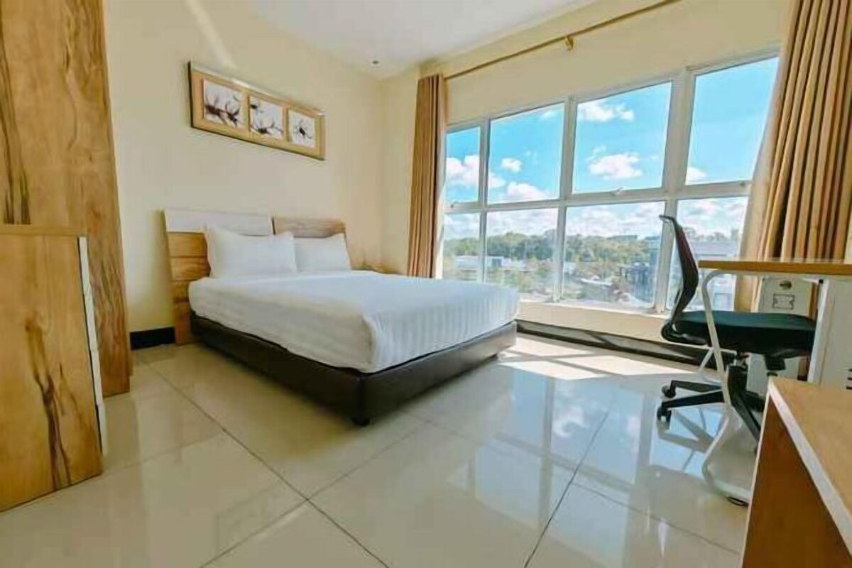 Habitación de hotel con cama, escritorio, silla y una ventana grande con vista a la ciudad.