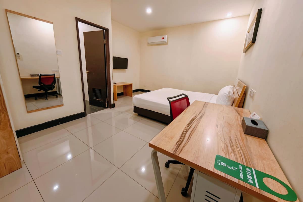 A hotel room with a bed, a desk, a chair, a mirror, a television, and a door.
