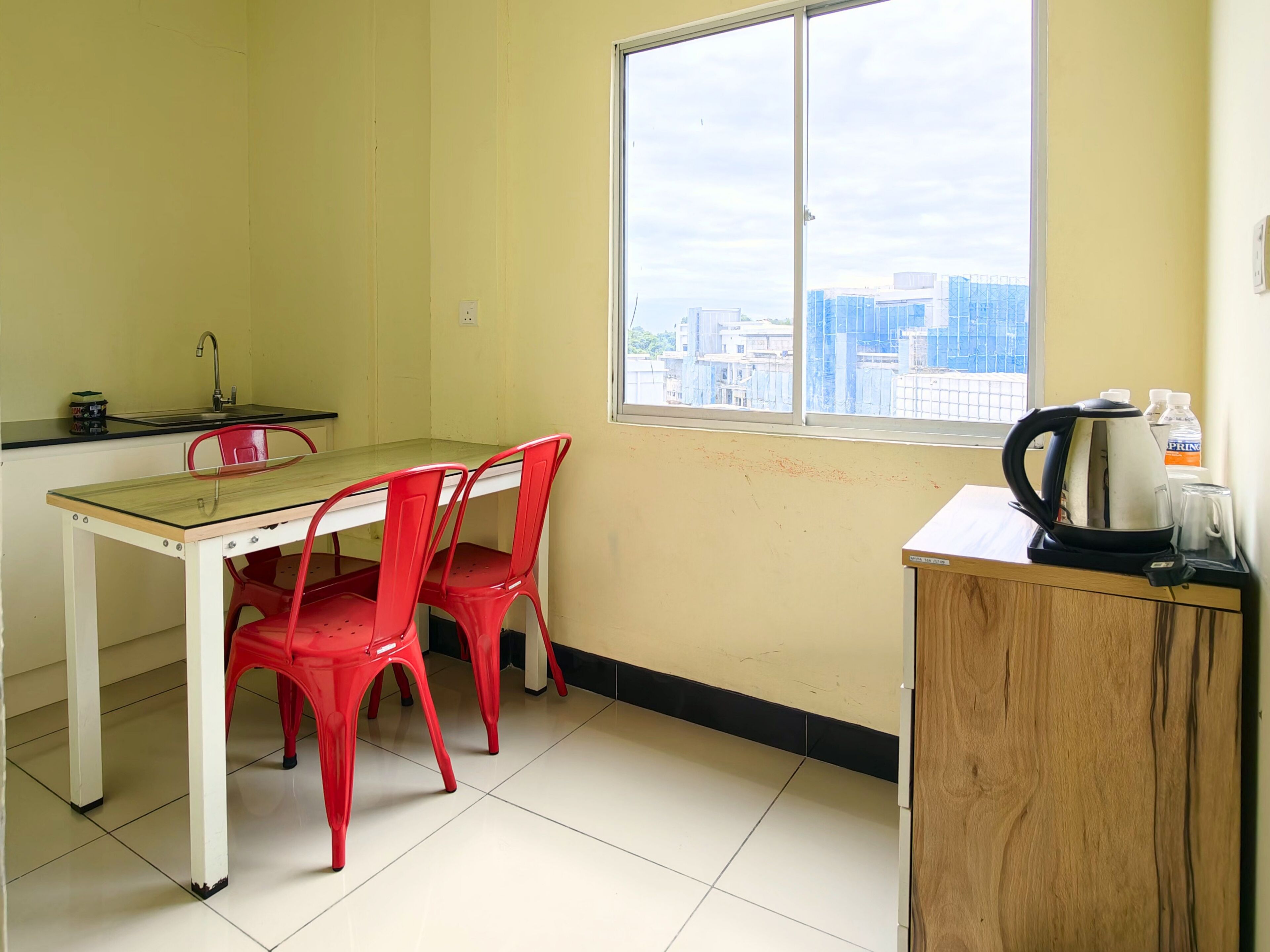 A small kitchen with a window, a table, two red chairs, and a coffee maker.