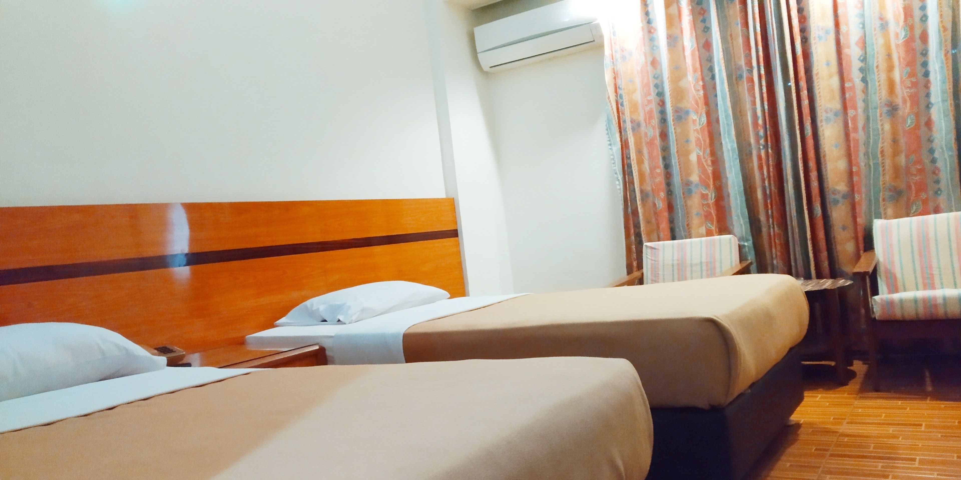 A hotel room with two beds, a wooden headboard, a chair, and a curtain.