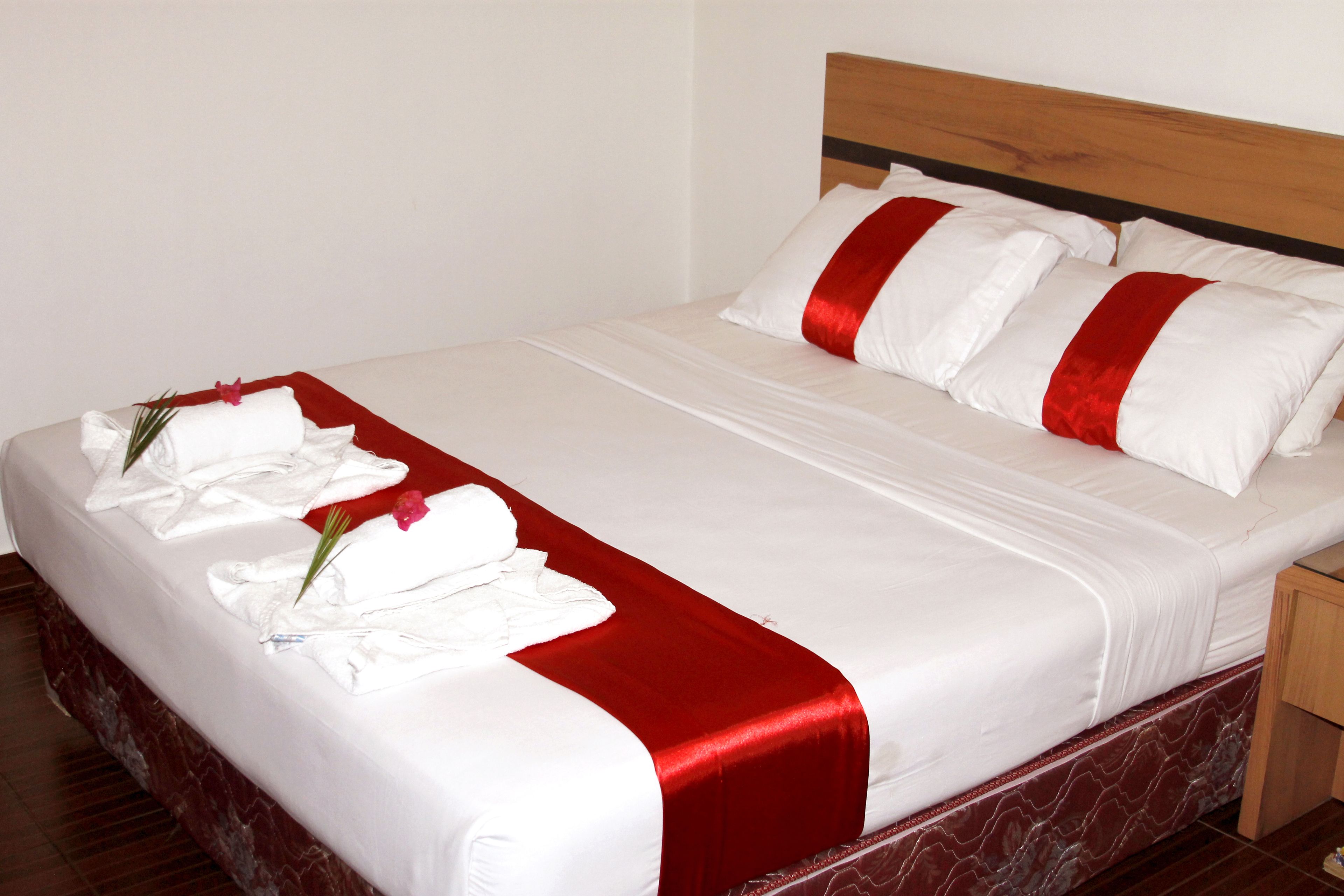 Un lit bien fait, avec du linge de lit blanc et rouge, une tête de lit en bois et une base de lit à motifs de marbre.