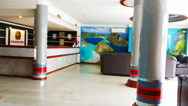 A hotel lobby with a reception desk, a mural of a tropical landscape, and seating areas. - Paradise Hotel (Tanjung Pinang)